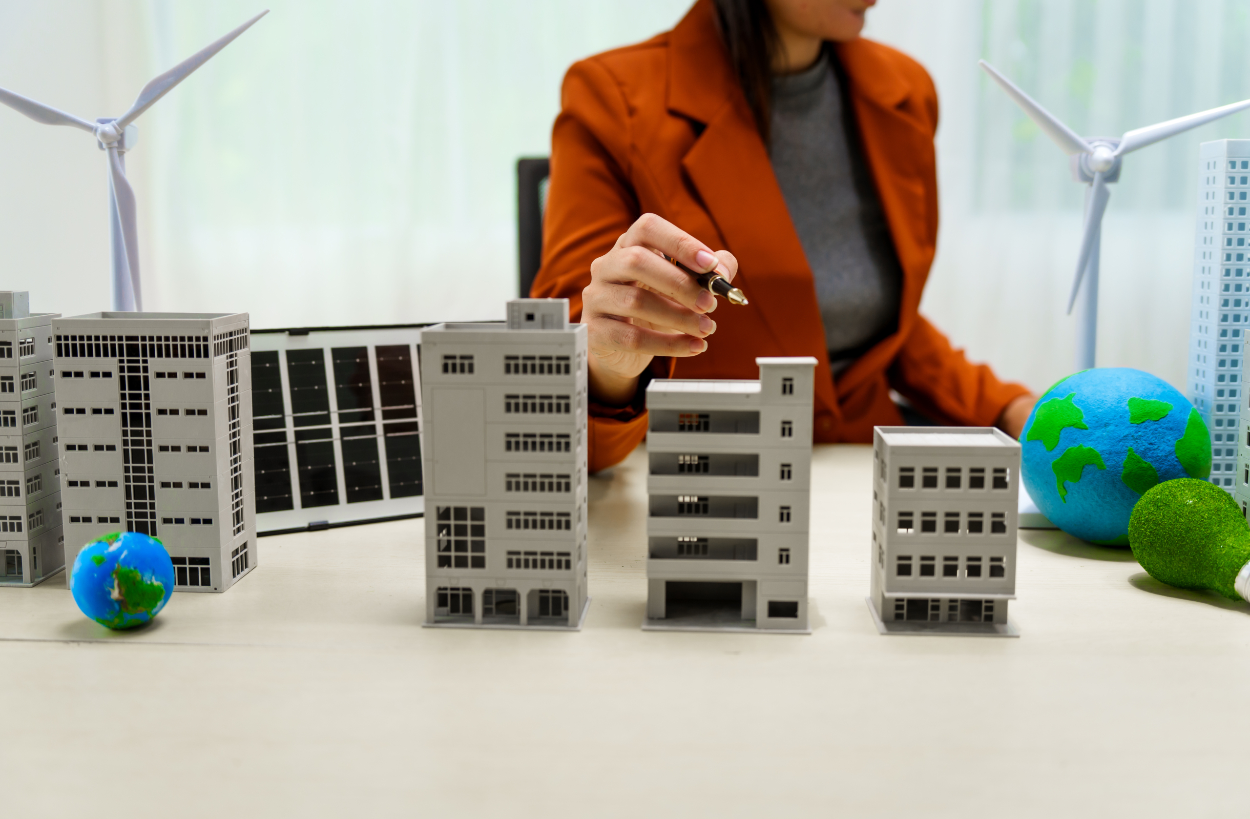 A businesswoman in a brown suit stands at a white desk with a world model